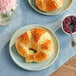 A Bridor curved vegan croissant on a plate with jam and flowers.