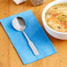 A bowl of soup and a Choice Bellwood stainless steel bouillon spoon on a napkin.