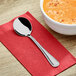 A Choice Milton stainless steel bouillon spoon on a red napkin next to a bowl of soup.