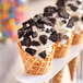 A waffle cone with Hydrox crushed cookie pieces on top of ice cream.