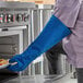 A person wearing a Tucker Safety blue oven mitt putting food into an oven.