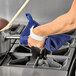 A person using a Tucker Safety blue poly-cotton hot pad to hold a pot with a wooden spoon over a stove.