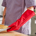A person wearing a red Tucker Safety oven mitt holding a tray of food.