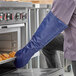 A person wearing a Tucker Safety blue oven mitt taking food out of an open oven.