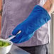 A person wearing a Tucker Safety blue oven mitt holding a pan of broccoli.