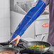 A person in a professional kitchen using a Tucker Safety blue nylon sleeve to cook over a stove.