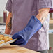 A person wearing a Tucker Safety blue oven mitt holding a tray of food.