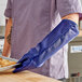 A person wearing a blue Tucker Safety puppet-style oven mitt holding a tray of food.