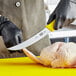 A person in black gloves using a Victorinox yellow Fibrox breaking knife to cut a chicken.