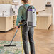 A man using a ProTeam backpack vacuum to clean a rug.