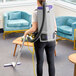 A woman using a white ProTeam backpack vacuum cleaner with a black hose to vacuum a room.