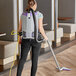 A woman using a ProTeam backpack vacuum to clean a room.