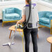 A woman using a ProTeam GoFit backpack vacuum cleaner to clean a room.