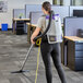 A woman using a ProTeam GoFit backpack vacuum to clean the floor in a corporate office cafeteria.