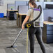 A person using a ProTeam backpack vacuum cleaner with a black rectangular attachment to vacuum a carpet.