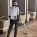 A woman using a ProTeam GoFit backpack vacuum cleaner to vacuum the floor in a corporate office cafeteria.