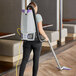 A woman using a ProTeam backpack vacuum to clean a restaurant kitchen.