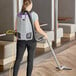 A woman holding a ProTeam GoFit backpack vacuum cleaner while vacuuming a wood floor.