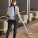 A woman using a ProTeam backpack vacuum to clean a carpeted floor.