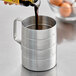 A person pouring liquid into a Choice aluminum measuring cup.