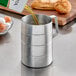 A person pouring olive oil into a silver aluminum measuring cup.