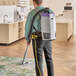 A man with a ProTeam backpack vacuum with a white and purple container vacuuming a carpet.