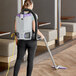 A woman using a ProTeam backpack vacuum cleaner to vacuum a room.