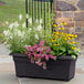 A Novelty Manufacturing Co. black rectangular patio planter with flowers in it.