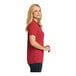 A woman wearing a rich red Port Authority short sleeve polo shirt.