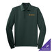A dark green Port Authority long sleeve polo shirt on a counter with gold embroidery.