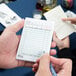 A person using a green and white Choice guest check to write on with a pen.