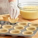 A person putting a Baker's Lane Kraft fluted cupcake wrapper into a muffin tin.