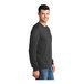A man wearing a Port & Company long sleeve T-shirt in dark heather gray.