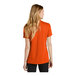 A woman wearing a Nike orange short sleeve polo with a v-neck.