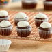 A group of cupcakes with white frosting in white fluted paper baking cups on a cooling rack.