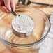 A person holding a measuring cup with a spoon over a bowl of flour.