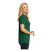 A woman wearing a deep forest green Port Authority Dry Zone short sleeve polo shirt.