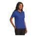 A woman wearing a royal blue Port Authority silk touch pique polo shirt.