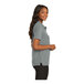 A woman wearing a Cool Gray Port Authority silk touch polo shirt with black buttons.