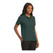 A woman wearing a dark green Port Authority silk touch polo shirt.