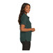 A woman wearing a dark green Port Authority silk touch polo shirt.