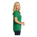 A woman wearing a bright kelly green Port Authority Dry Zone polo shirt.