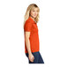 A woman wearing a deep orange Sport-Tek polo shirt.