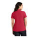 A woman wearing a Port Authority red short sleeve polo shirt.