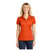 A woman wearing a deep orange Sport-Tek short sleeve polo shirt.