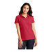 A woman wearing a rich red Port Authority pique polo shirt.
