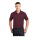 A man wearing a maroon Sport-Tek short sleeve polo shirt.