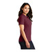 A woman wearing a Port Authority burgundy short sleeve polo shirt.