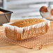 A loaf of bread in a white fluted oblong loaf liner on a cooling rack.