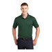 A man wearing a forest green Sport-Tek short sleeve polo.